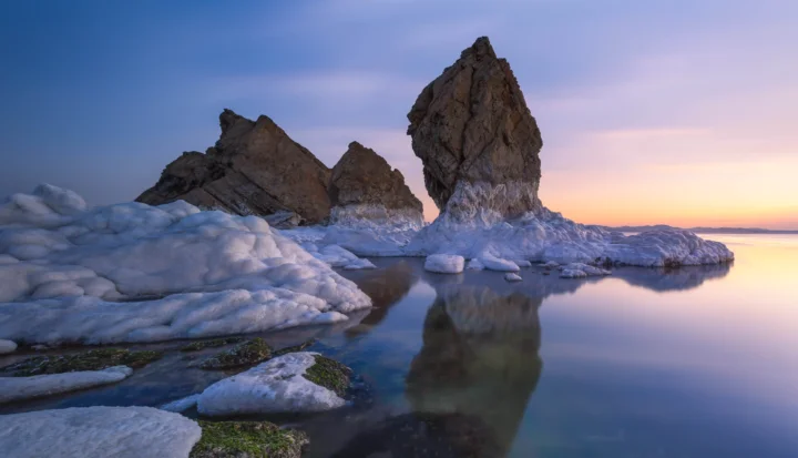 暮色天空下，冰川湖泊映照着耸立的岩峰与冰雪岸线。