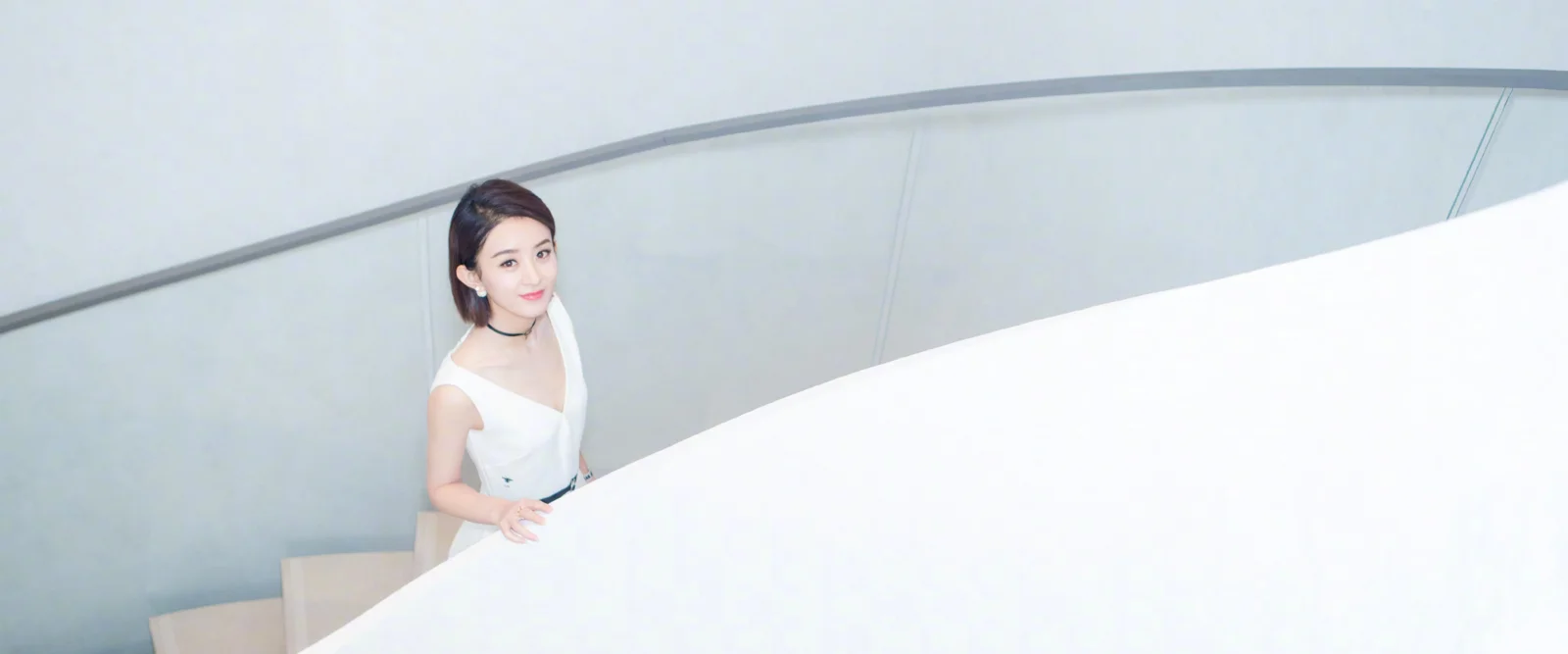 一名女子站在明亮的白色弧形楼梯旁。