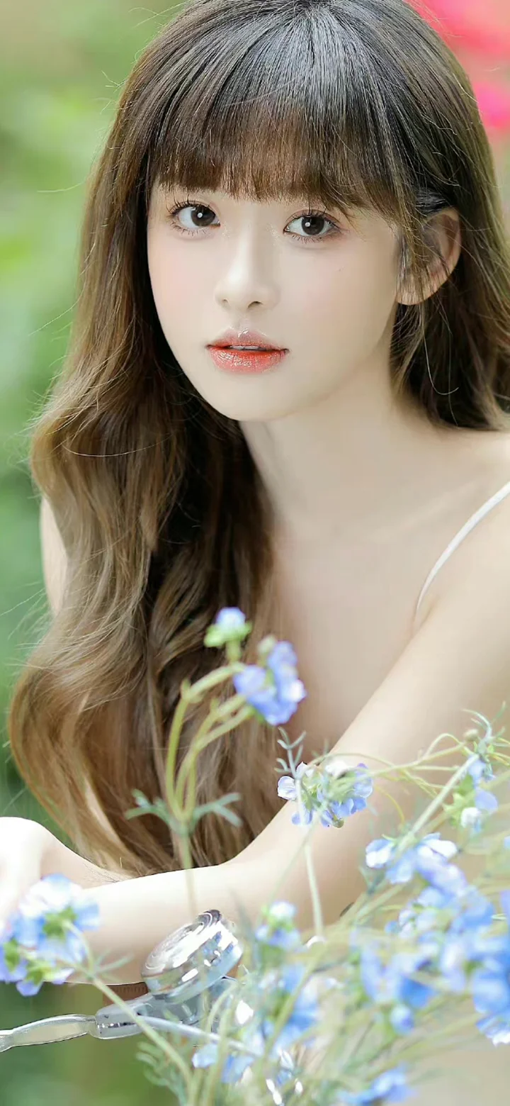 一位长发女子手持蓝色花朵的近距离人像照片。