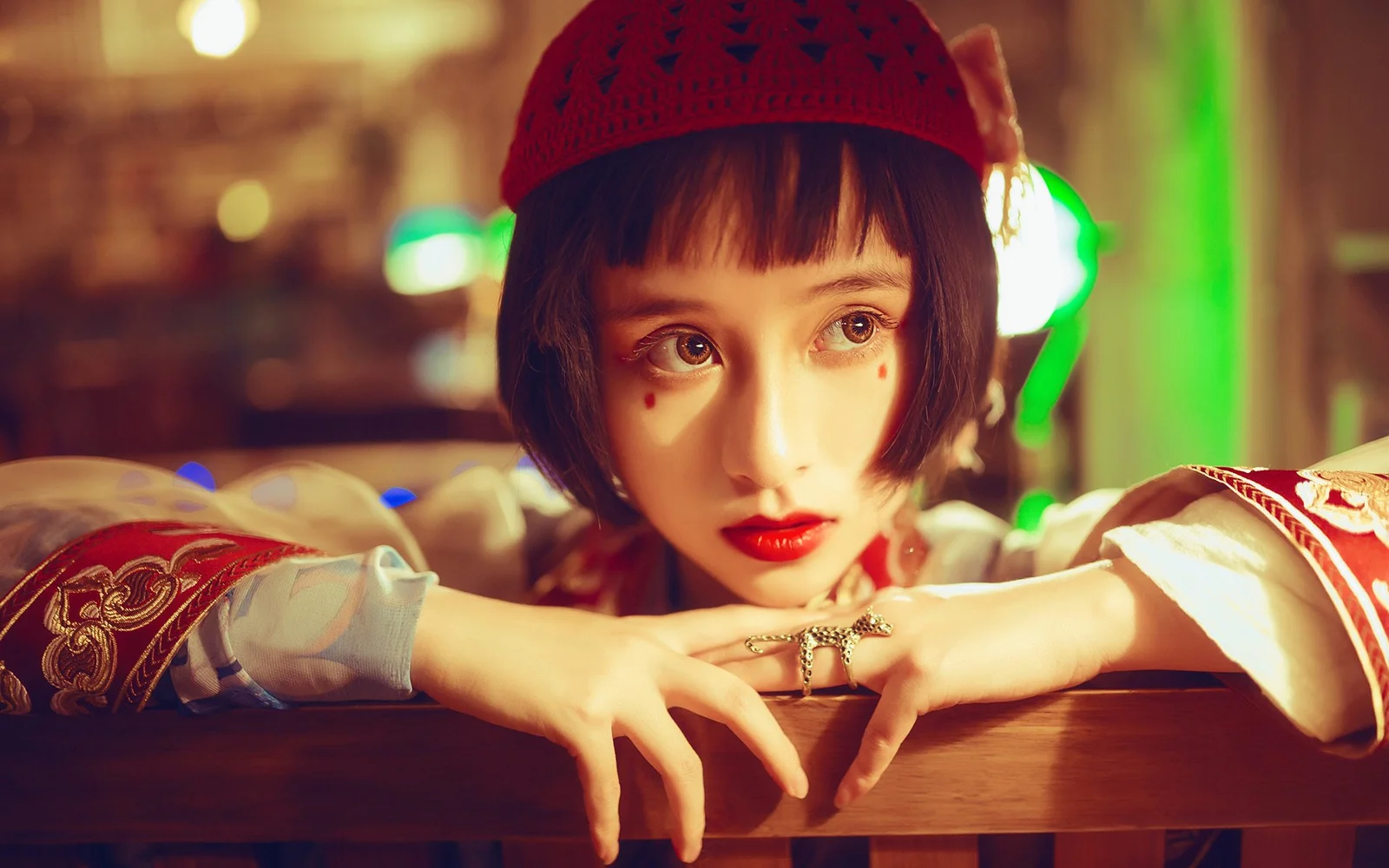 빨간 니트 모자를 쓴 여성이 따뜻한 조명 아래 나무 테이블에 기대고 있습니다.