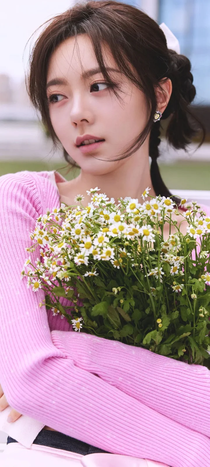 一名女子穿着粉色针织衫，怀抱一大束白色小雏菊。