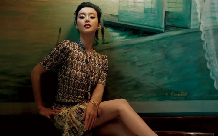 一名成年女性身穿图案连衣裙坐在绿色调背景前。