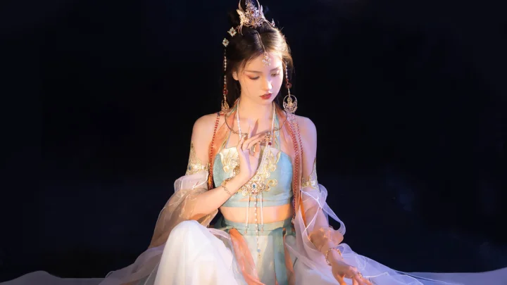 一名身着华丽传统服饰并佩戴精致头饰的女子坐在深色背景前。