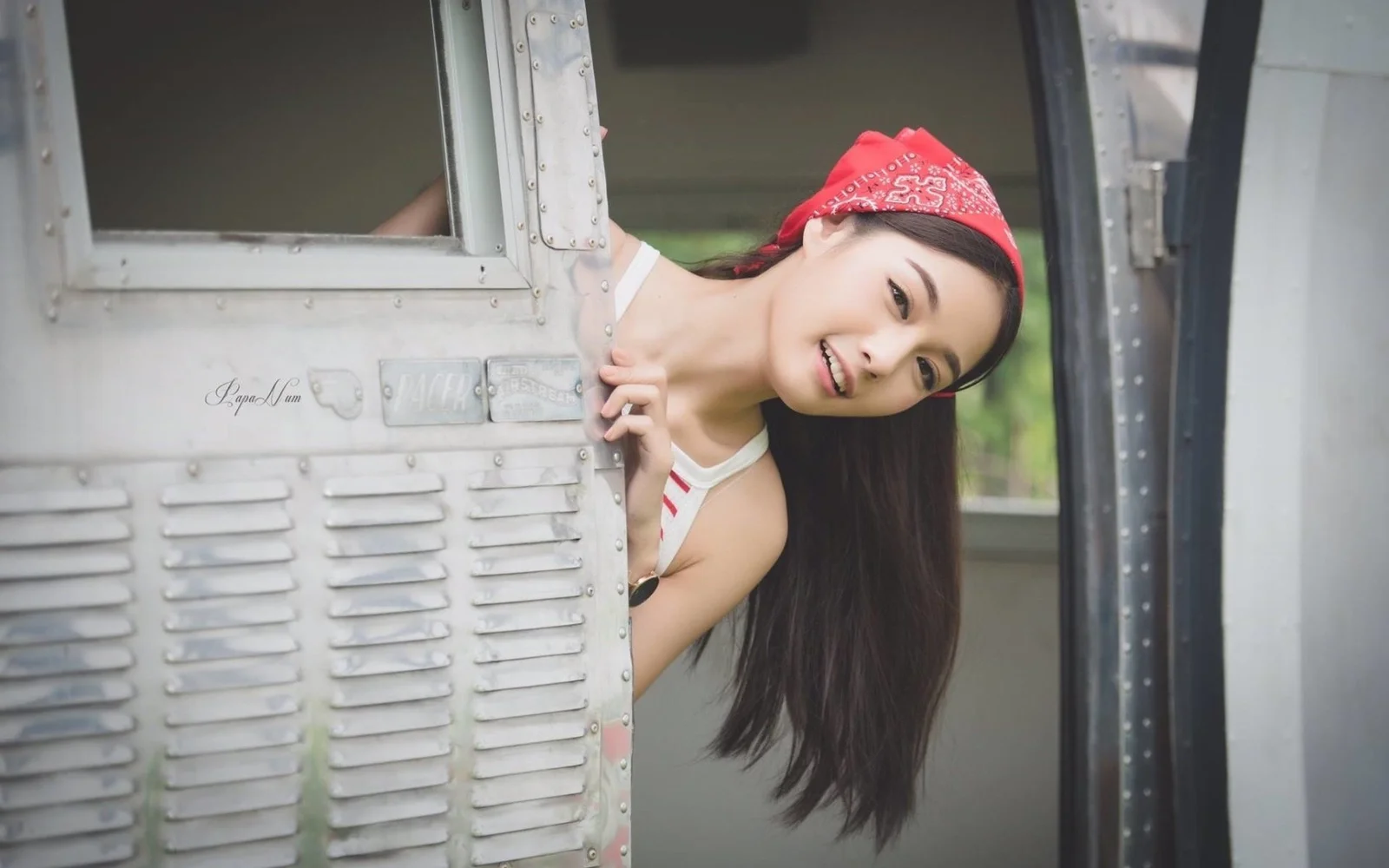 一名戴著紅色頭巾的女子從銀色車門後探出身子微笑。