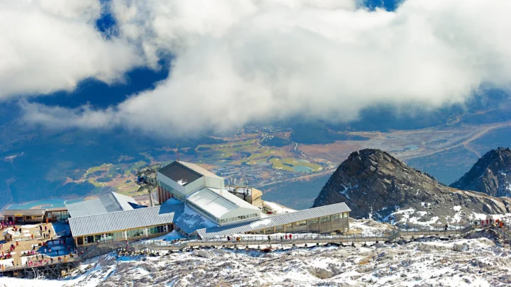 雪覆盖的高山度假区坐落在群峰之间，云层下方可见远处的山谷与田野。