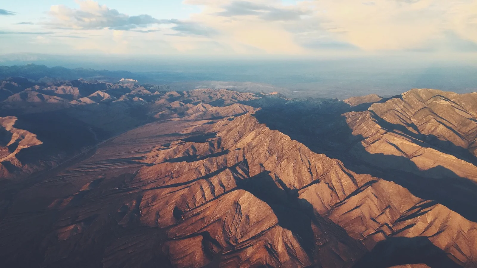 空撮によって、暖かな光に照らされた連なる山々の稜線と深い谷が映し出されています。