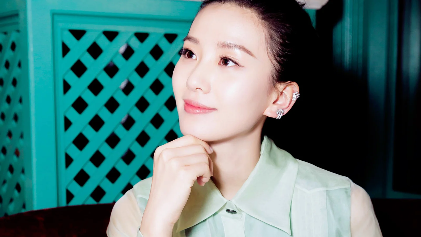 一名女性靠在手上，面带微笑，身后是青绿色格栅背景。