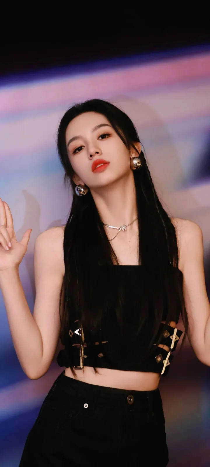一名長髮女性身穿黑色無袖上衣，在彩色虛化背景前面對鏡頭。