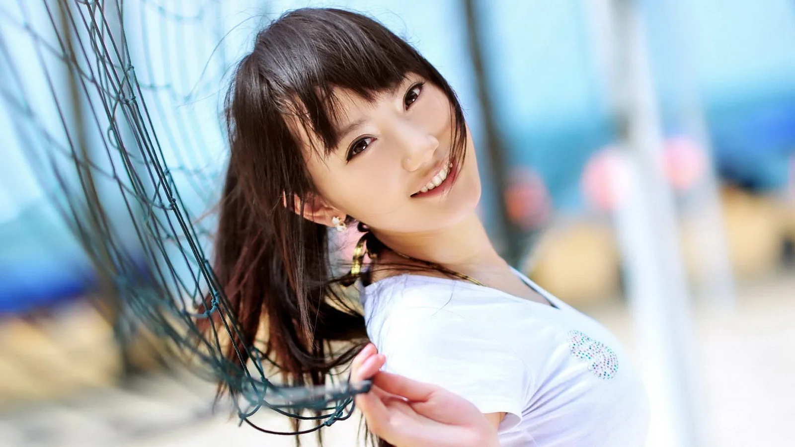 明るくぼかされた背景の中で、笑顔の成人女性がスポーツ用ネットのそばに立っています。