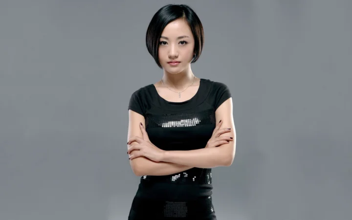 一名成年女性穿着黑色上衣，在灰色背景前交叉双臂进行棚拍肖像。