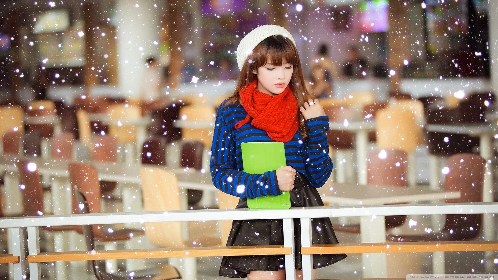 白いニット帽と赤いマフラーを身につけた女性が、雪の降る室内空間に立っています。