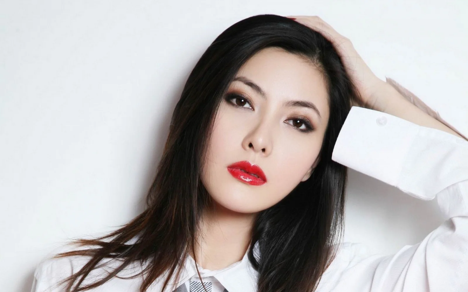 一名长发女性身穿白衬衫，在白色背景前摆出肖像姿势。
