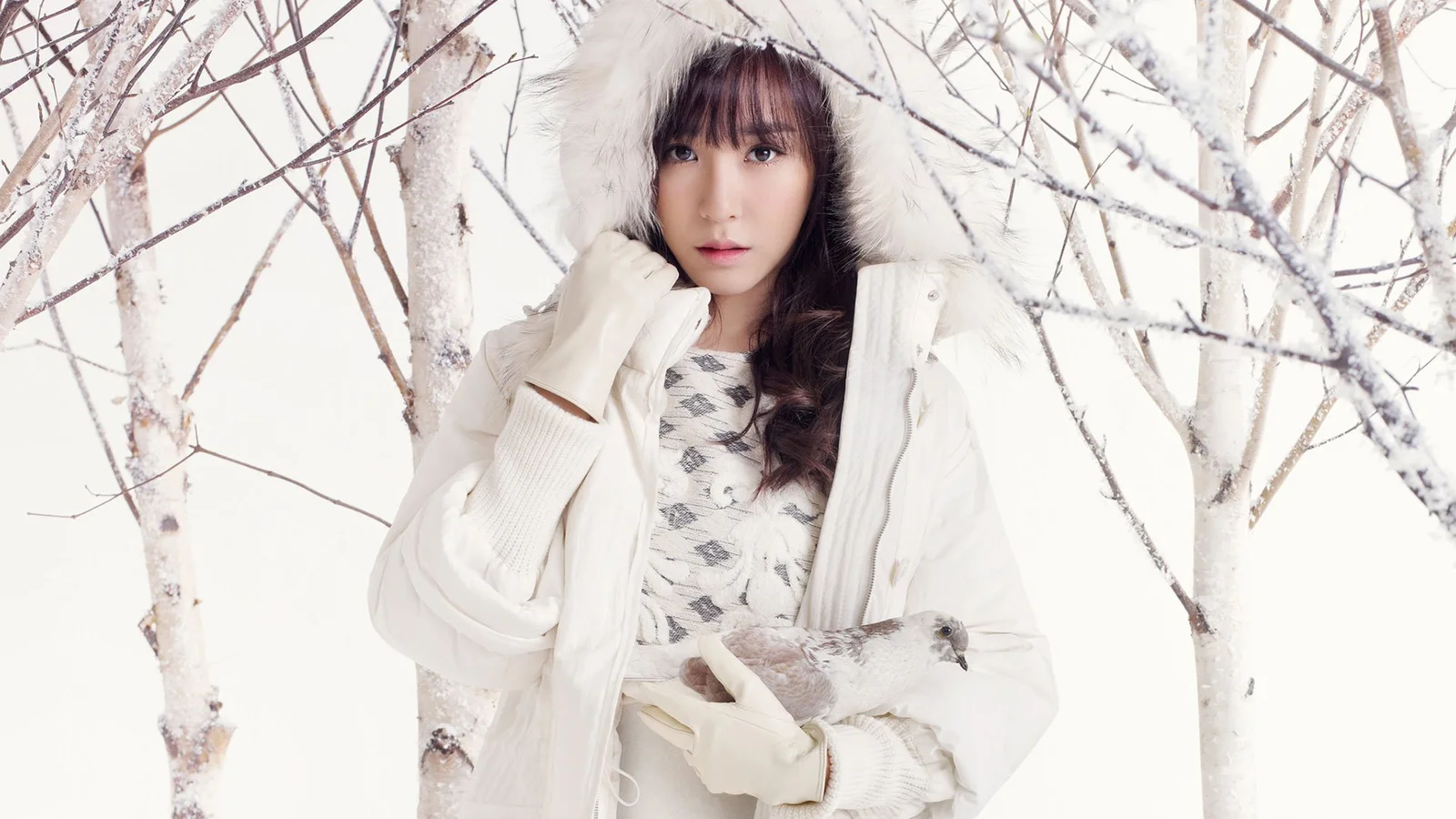 一位穿着白色冬装的女性站在白桦树与积雪之间。