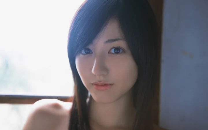一位长发女性在窗边的近距离肖像，柔和光线映照着她的脸庞。