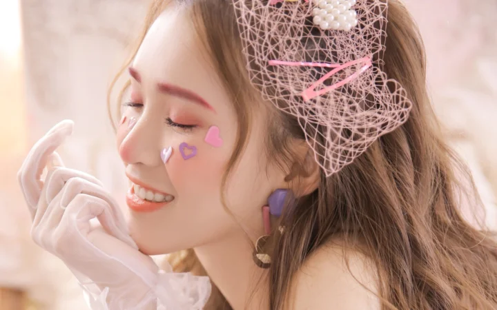 핑크 메이크업과 화려한 헤어 액세서리, 흰 장갑을 착용한 여성의 미소 짓는 옆모습 인물 사진。