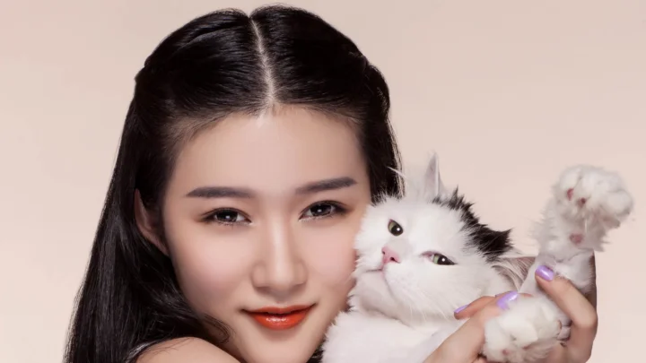 一名成年女子抱着一只白色猫咪面对镜头。