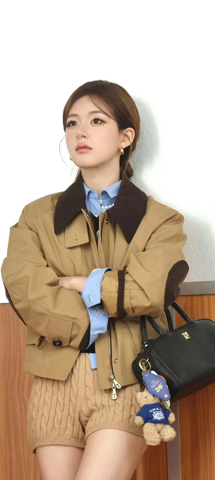 一名女子穿着棕色外套和蓝色衬衫，抱臂坐在室内。