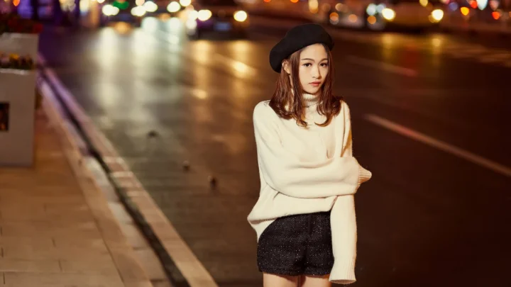 一名戴贝雷帽的女子站在夜晚灯光映照的城市街道旁。
