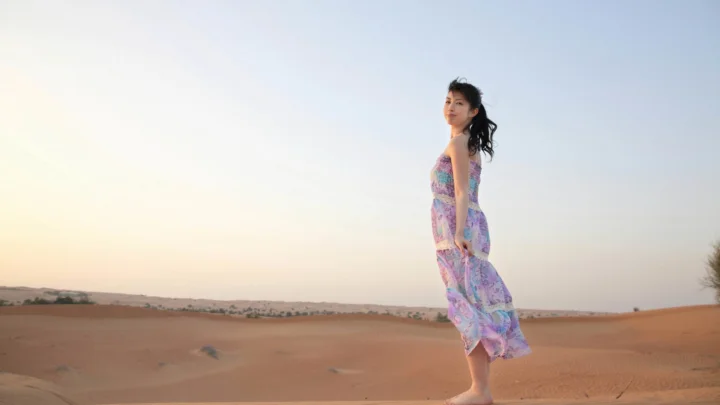 一名身穿彩色长裙的女子站在夕阳映照的沙漠中。