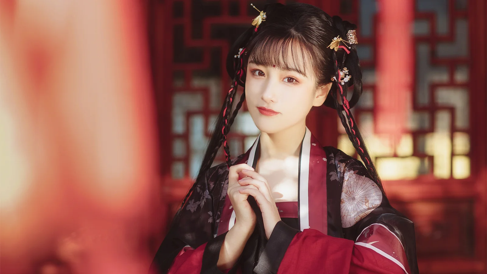 一名身穿中式传统服饰的女子站在红色装饰背景前。