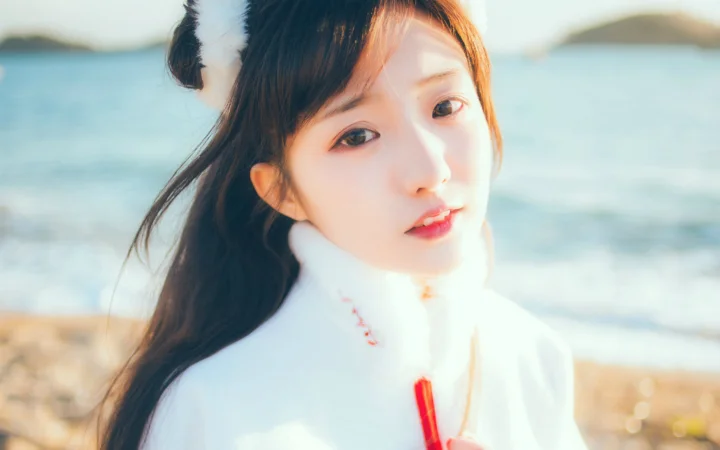 一名身穿白衣的女子在海边明亮的光线下看向镜头。
