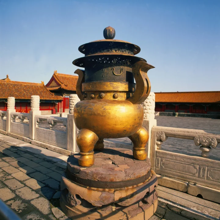 阳光下的巨大青铜器矗立在红墙金瓦的宫殿庭院中。