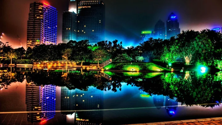 夜色中的城市高楼、灯光璀璨的公园与平静水面倒映出绚丽的霓虹光影。