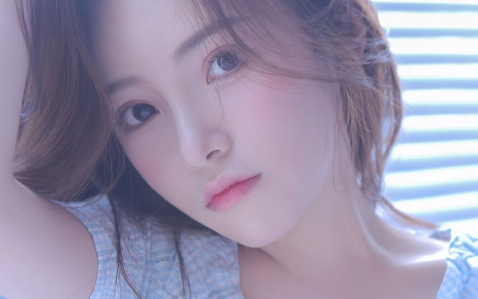부드러운 빛을 받는 성인 여성의 얼굴을 담은 클로즈업 인물 사진으로, 배경에 가로 블라인드가 보인다.