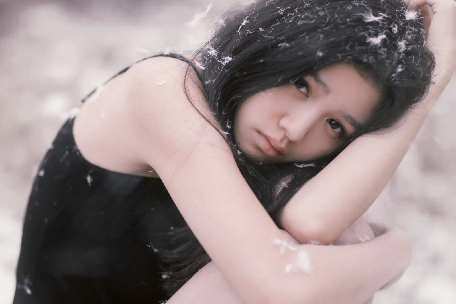 一名黑发女性以手臂支撑头部，面向镜头呈现柔和的肖像画面。