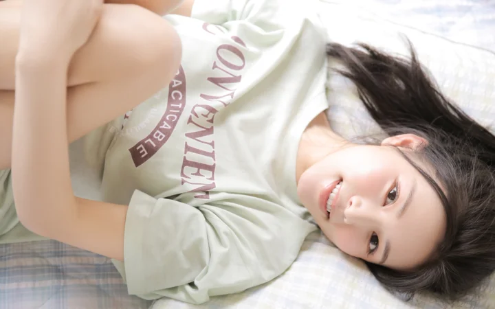 一名长发女子穿着浅色T恤躺在床上微笑看向镜头。