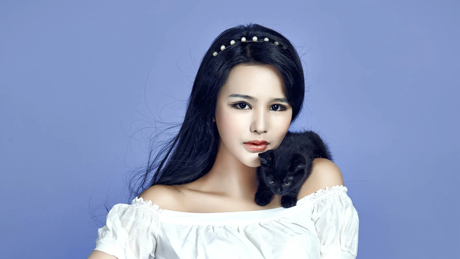 一名长发女子身穿白色露肩上衣，肩上抱着一只黑猫，背景为纯蓝色。