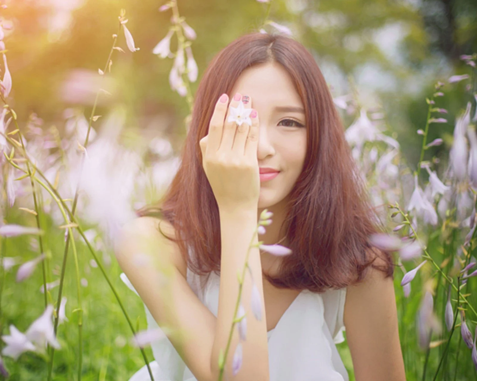 一名女子站在花丛中，用手遮住一只眼睛。