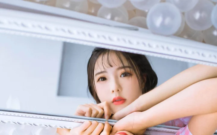 一名成年女性从装饰镜框后望向镜头，背景为浅色室内光影。