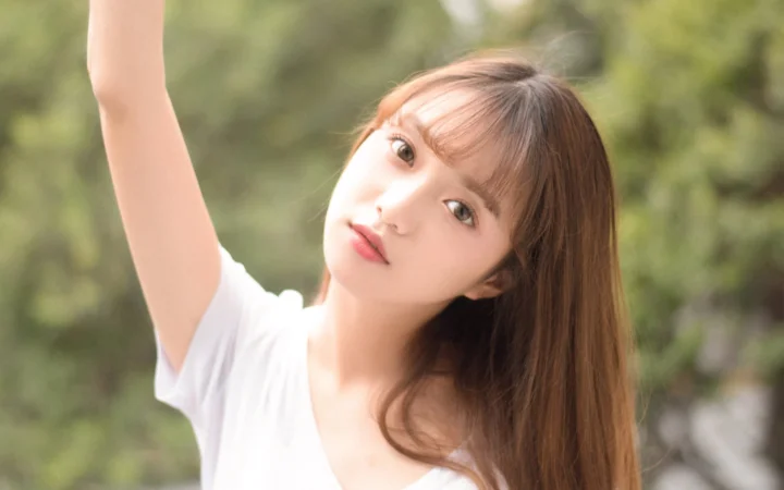 긴 머리의 여성이 초록빛 배경 앞에서 팔을 들어 카메라를 바라보고 있습니다.