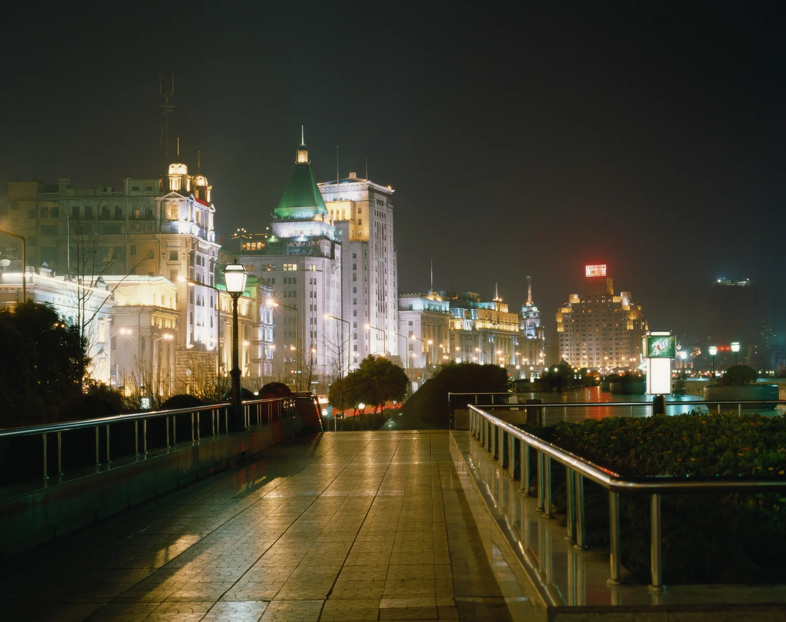 夜晚灯火映照着滨水步道、城市建筑与平静水面。