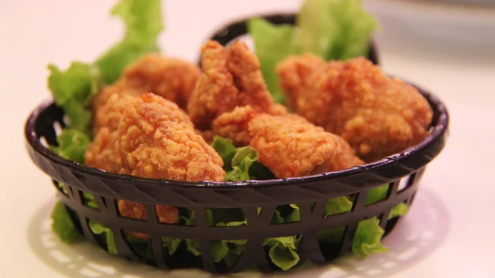 黑色篮子里装着金黄酥脆的炸鸡块，周围点缀着绿色生菜。