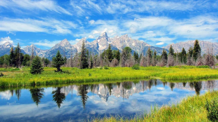 蓝天白云下的群山、森林与湖泊倒影构成宁静的自然风景。
