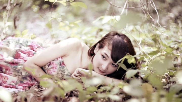 성인 여성이 나뭇잎과 낙엽 사이에 누워 카메라를 바라보고 있다.