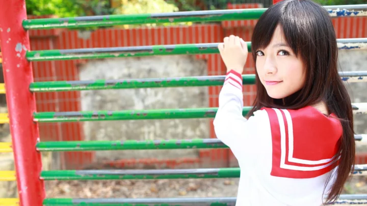 一名穿红白水手服的女性站在绿色栏杆旁回望镜头。
