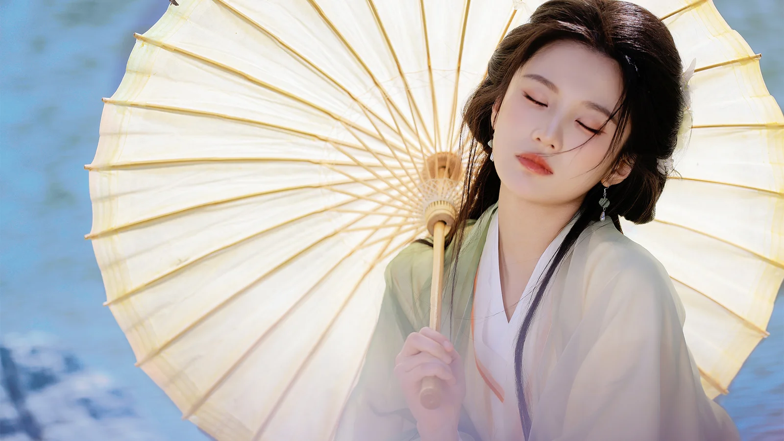 一名身穿淺色服裝的女子閉眼手持油紙傘，藍色背景映襯著她的側身。