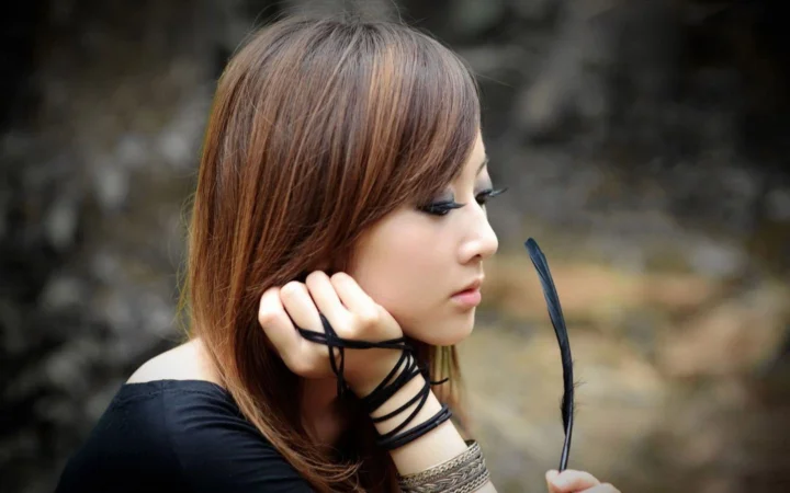 茶色の長い髪の女性が屋外で横顔を見せ、黒いサングラスを手にしています。