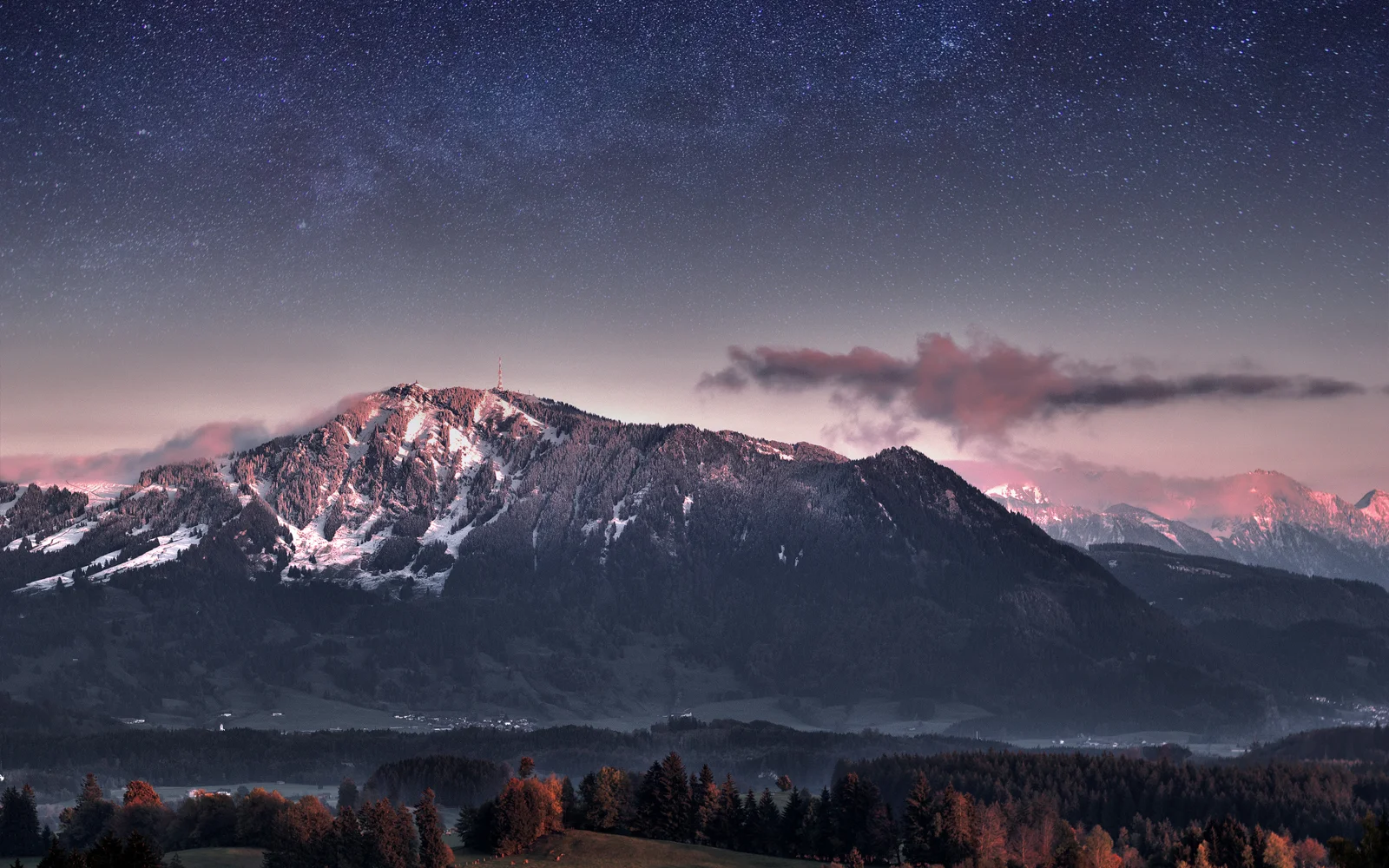 夜空下的积雪山脉延伸 across the dark forested foreground。