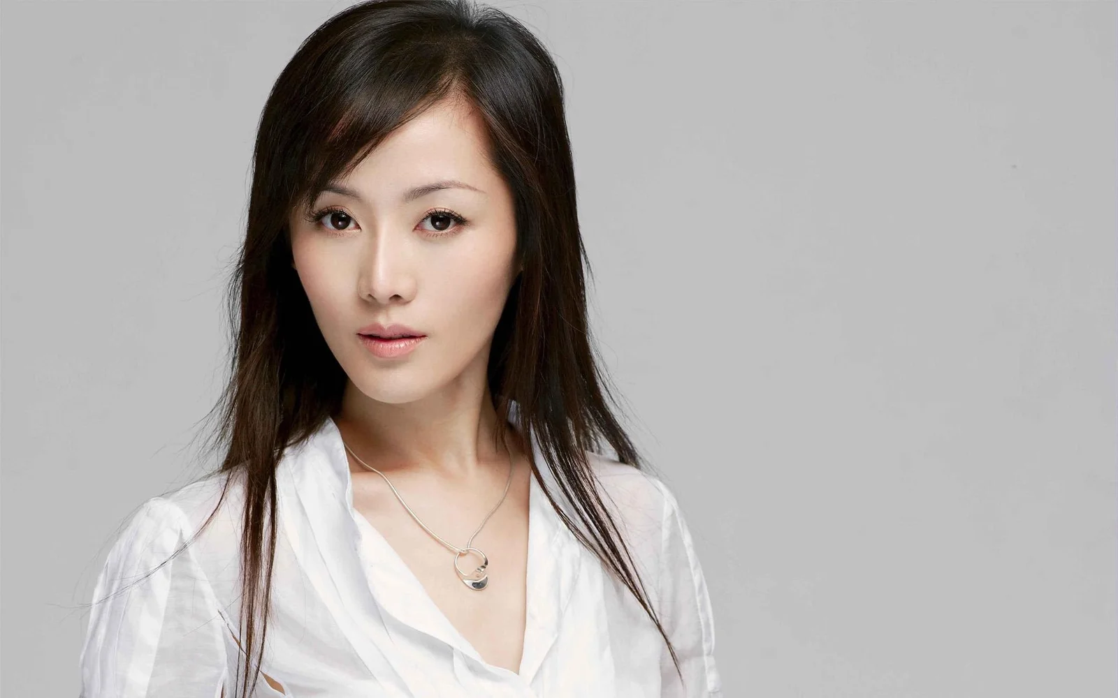 흰색 블라우스를 입은 성인 여성이 회색 배경 앞에서 스튜디오 인물 사진을 촬영하고 있다.