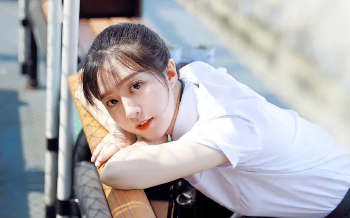 一名身穿白色上衣的女子俯身靠在木欄上看向鏡頭。