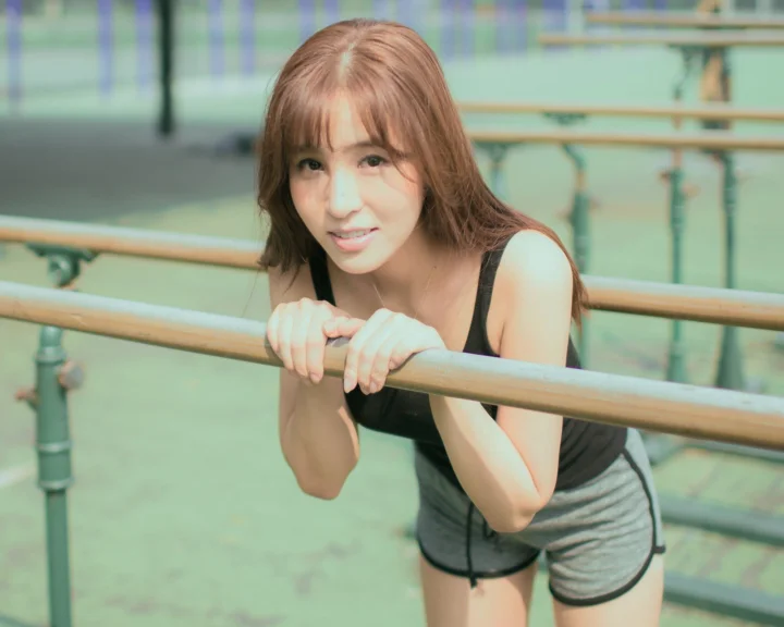 一名成年女性在室内健身房栏杆旁微笑看向镜头。