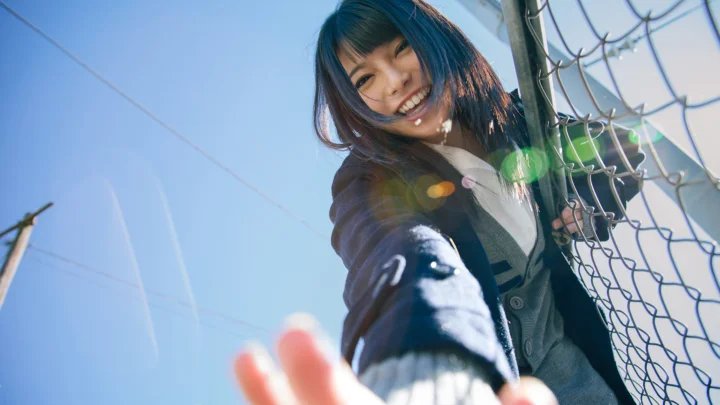 一名短发女子在蓝天下靠近铁丝网微笑伸手。
