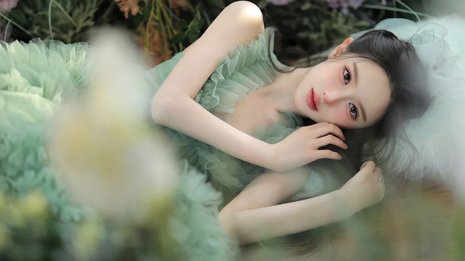 一名身穿薄荷绿色纱裙的女子侧躺在柔和的植物背景中。