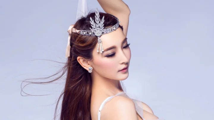 一名佩戴华丽头饰的成年女性在浅紫色背景前侧身摆 pose。