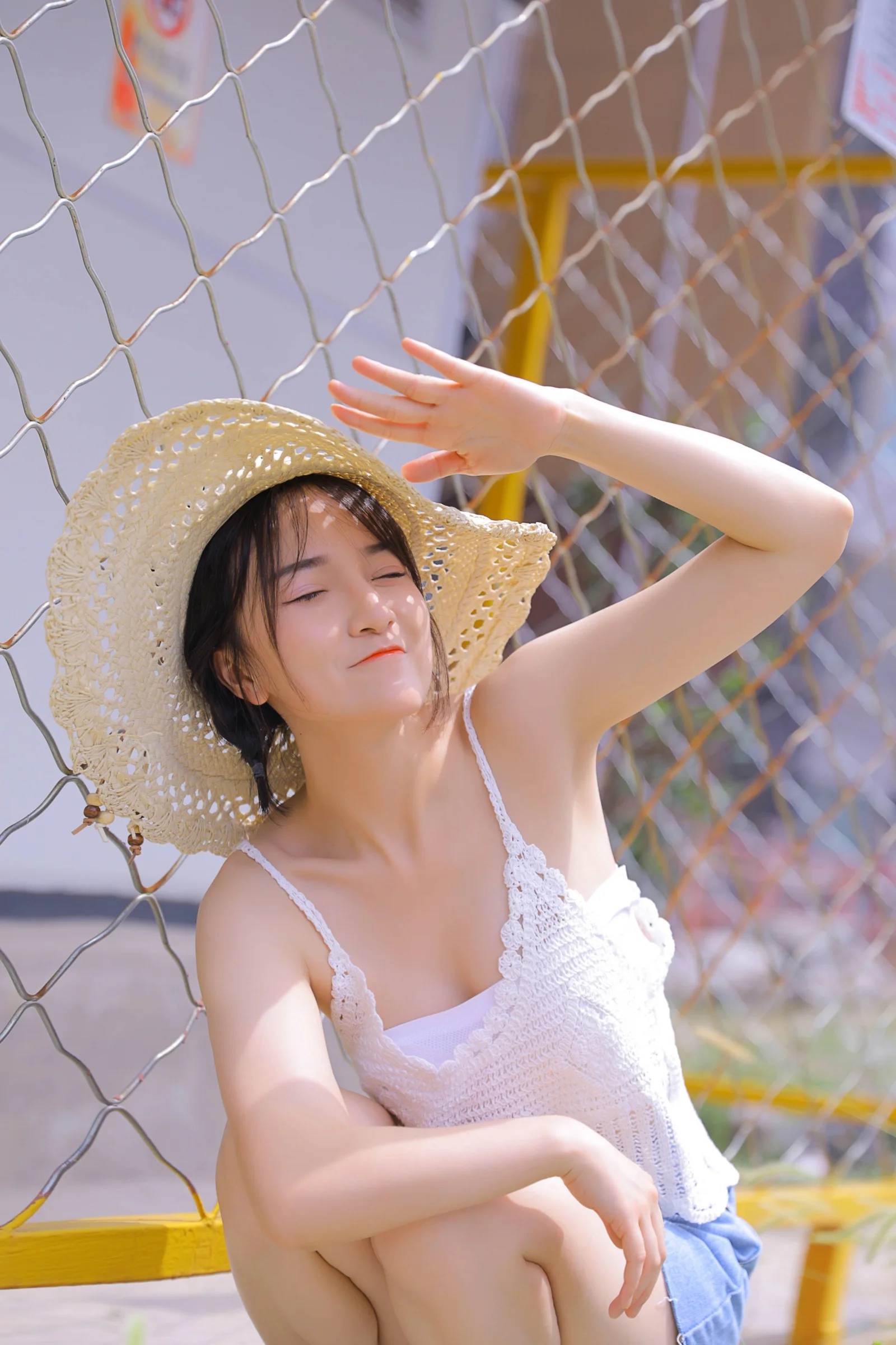 一名戴草帽的女性在户外围网旁闭眼微笑。