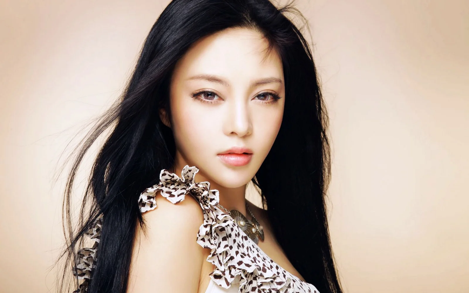 一名黑发女性面对镜头进行室内肖像拍摄，背景为浅色调。